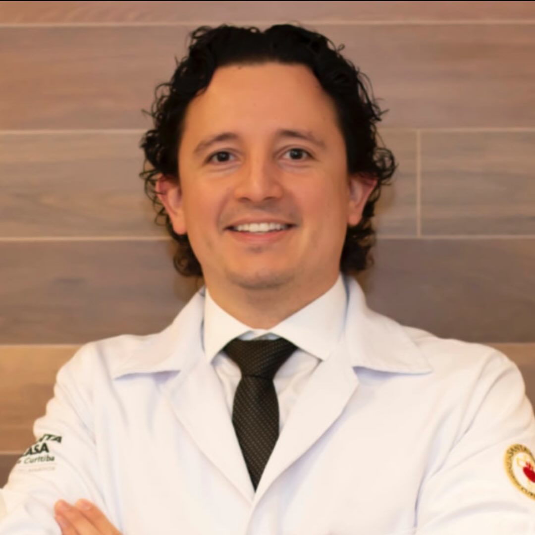Dr. Fernando sorrindo e olhando para a câmera, de braços cruzados e vestindo jaleco branco.