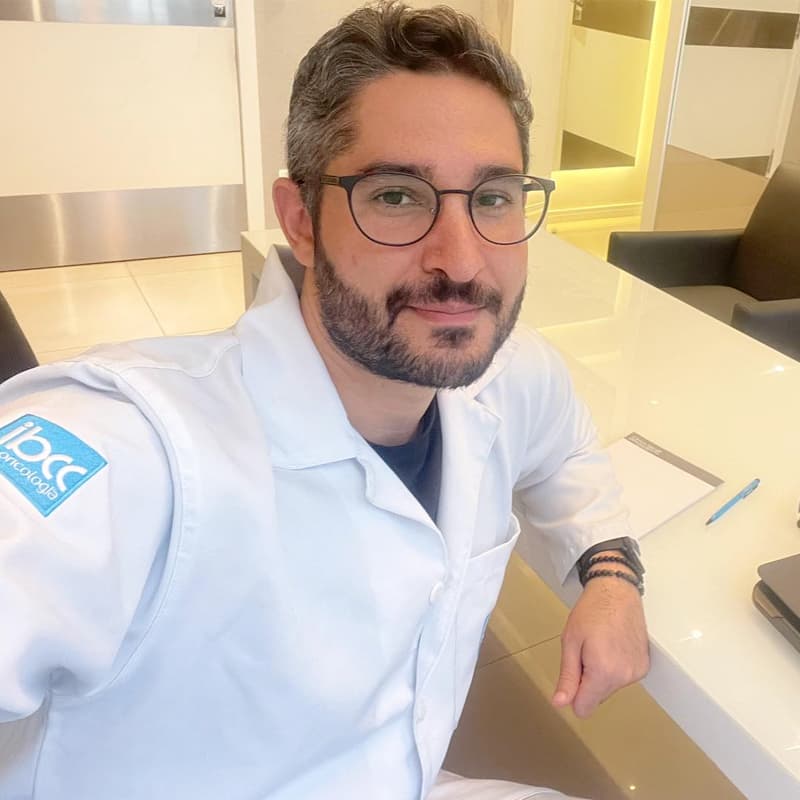 Dr. João Abelha olhando para a câmera e sorrindo discretamente, sentado em seu consultório e vestindo jaleco branco.