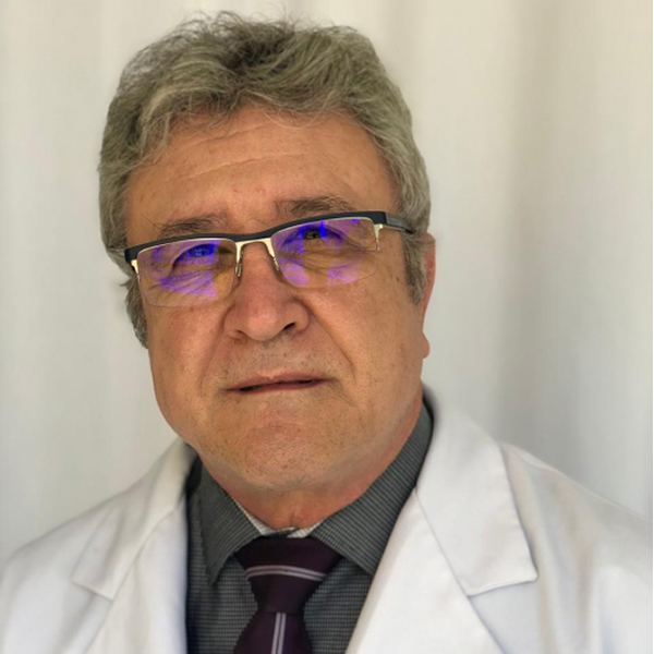 Dr. Francisco, levemente sorrindo e olhando para a câmera, vestindo uma camisa cinza, gravata e jaleco branco.