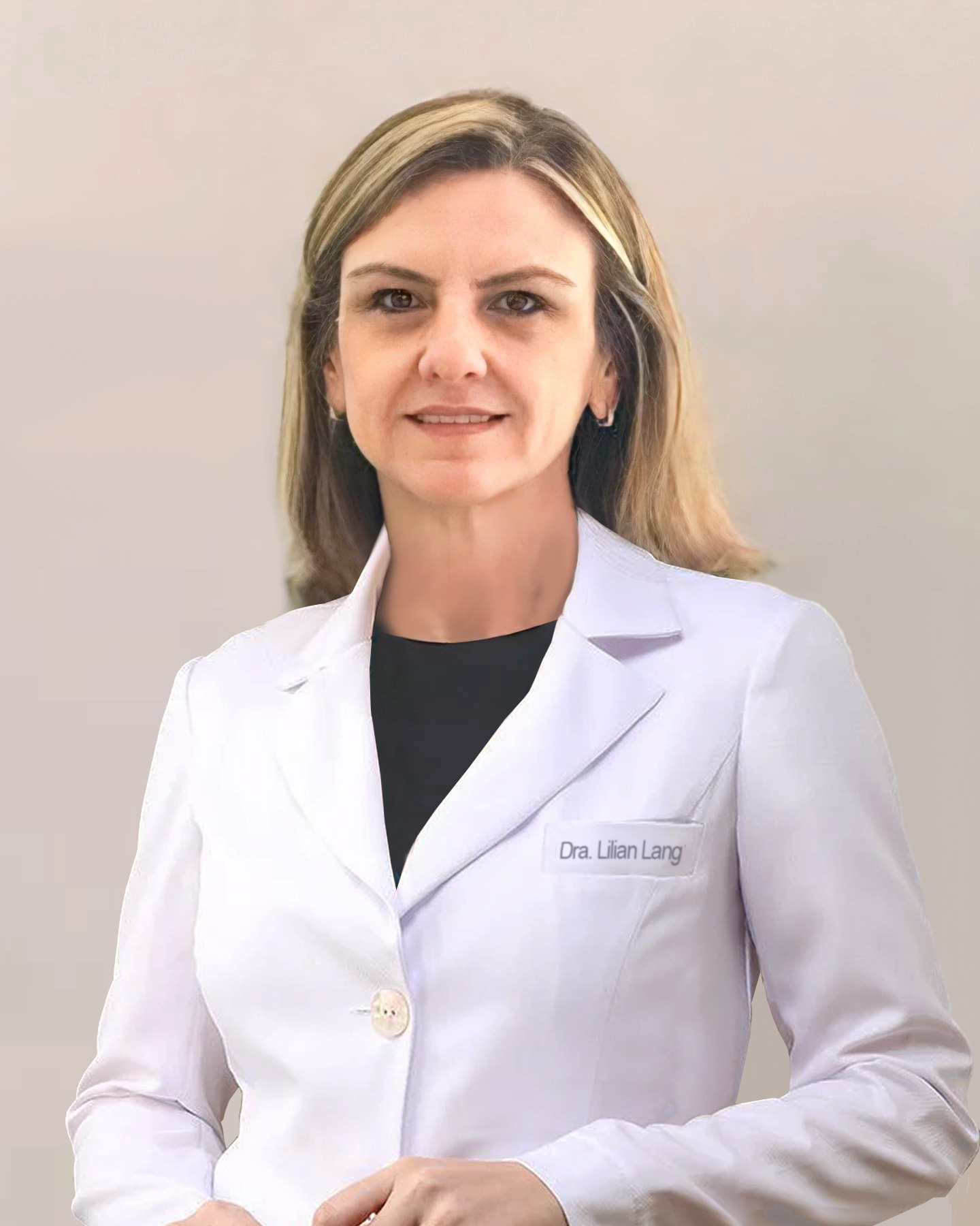 Dra. Lilian Regina Lang, ginecologista em Curitiba, meia idade, cabelos até os ombros, loiros e lisos, está de pé, com as mãos juntas, sorrindo e olhando para a câmera, aparentemente em seu consultório, ela está vestindo uma camiseta preta com um jaleco branco por cima, por trás uma parede bege.