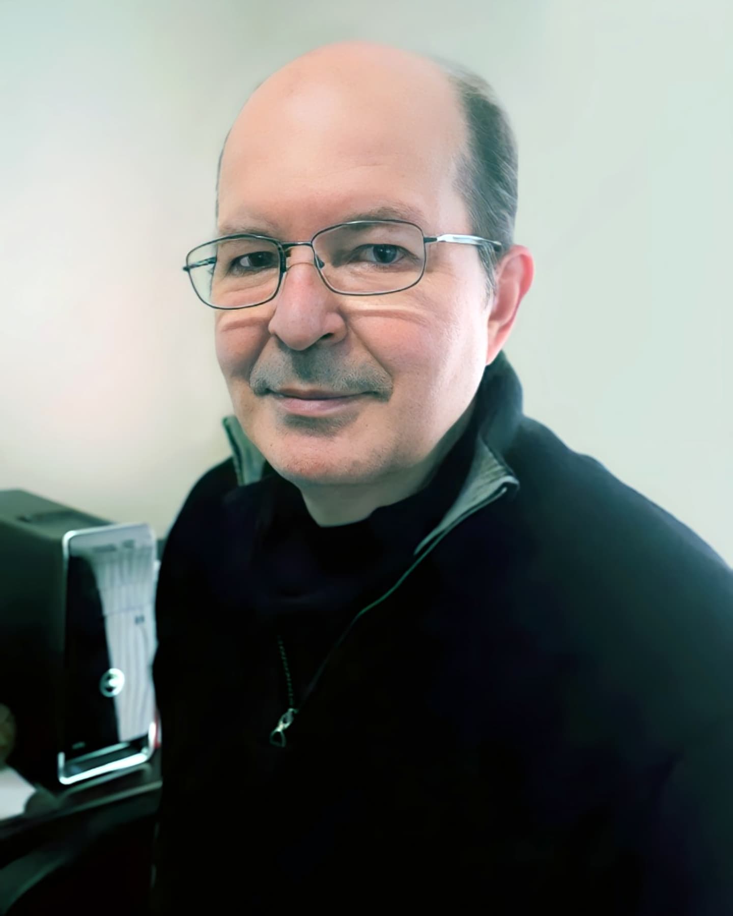 Foto do Dr. Rui Max Beckhauser, Psiquiatra em Curitiba. Ele aparece em seu consultório profissional, usando óculos e uma blusa escura, transmitindo uma imagem de seriedade e confiança. Ao fundo, há um computador e um ambiente bem iluminado, sugerindo seu espaço de trabalho.
